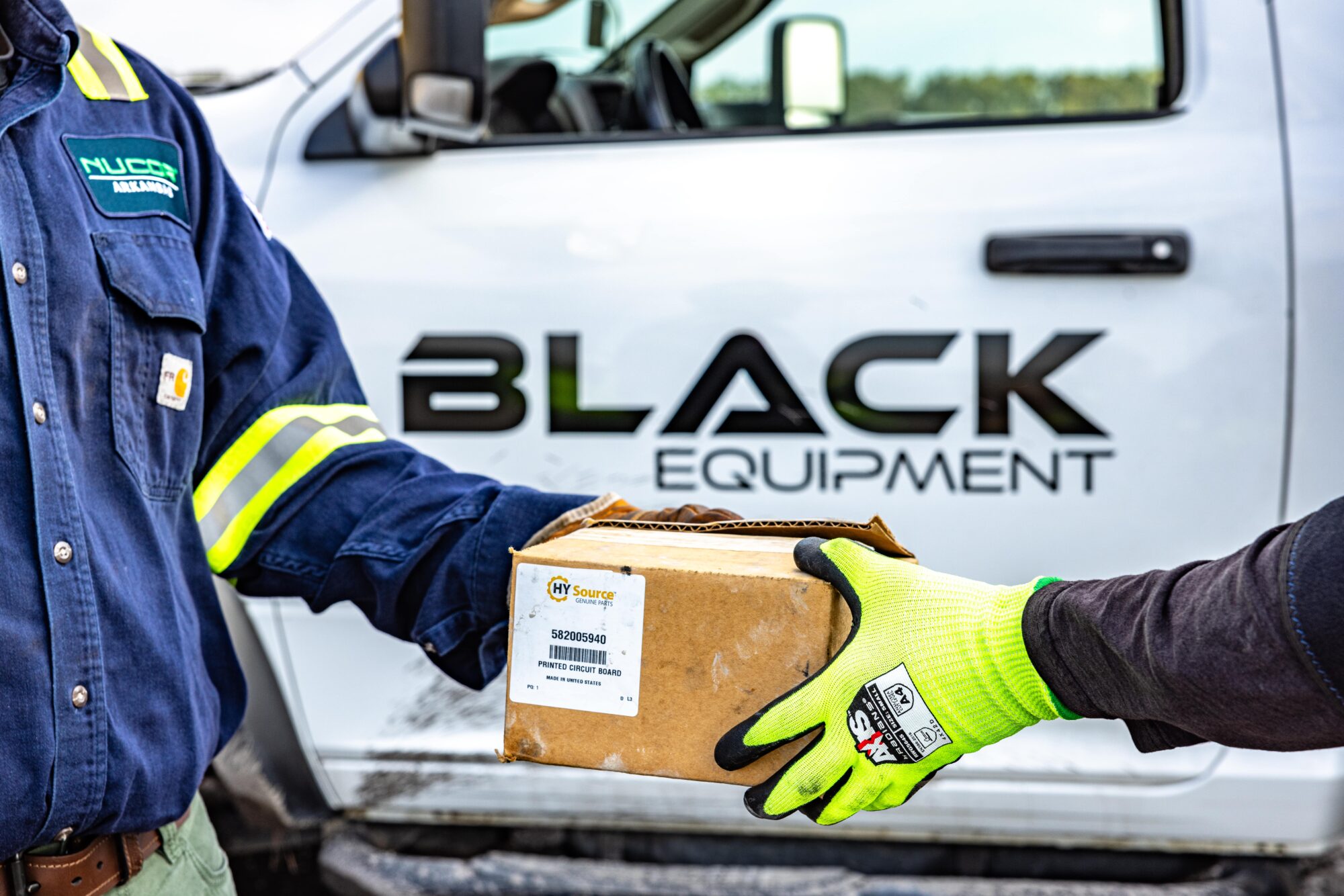 Employee handing customer a box of parts in front of a Black Equipment branded vehicle