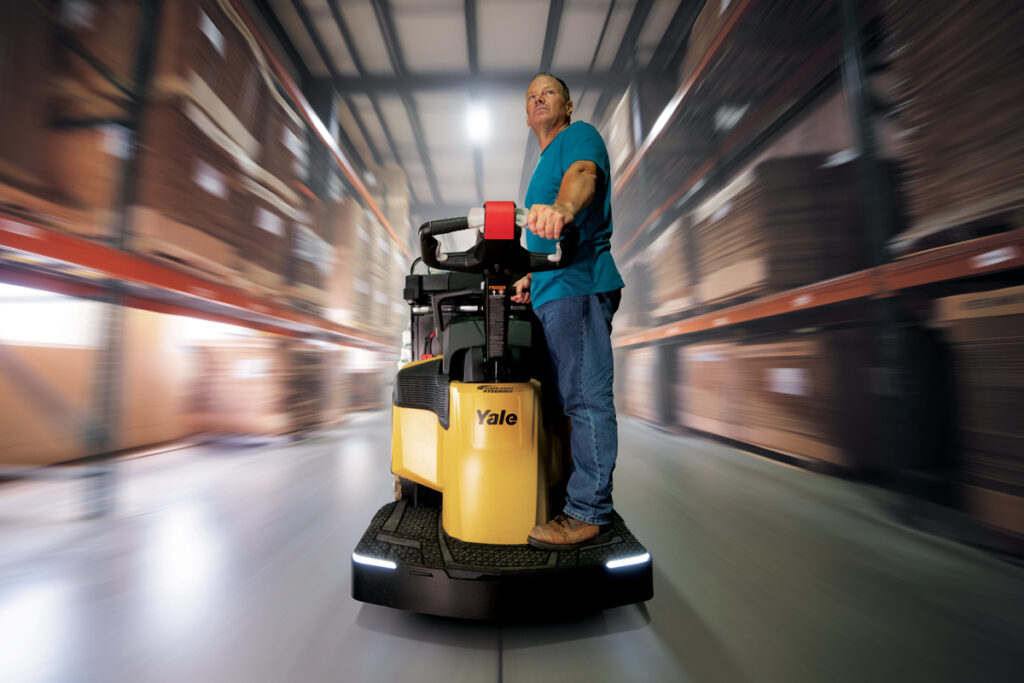 zooming through a warehouse on electric ride-along tow tractor (forklift) and shelving.