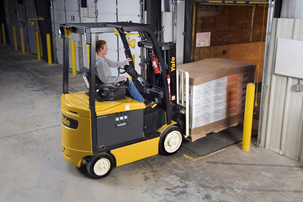 Electric counterbalanced forklift loading a skid of product onto a trailer inside a warehouse/3PL.
